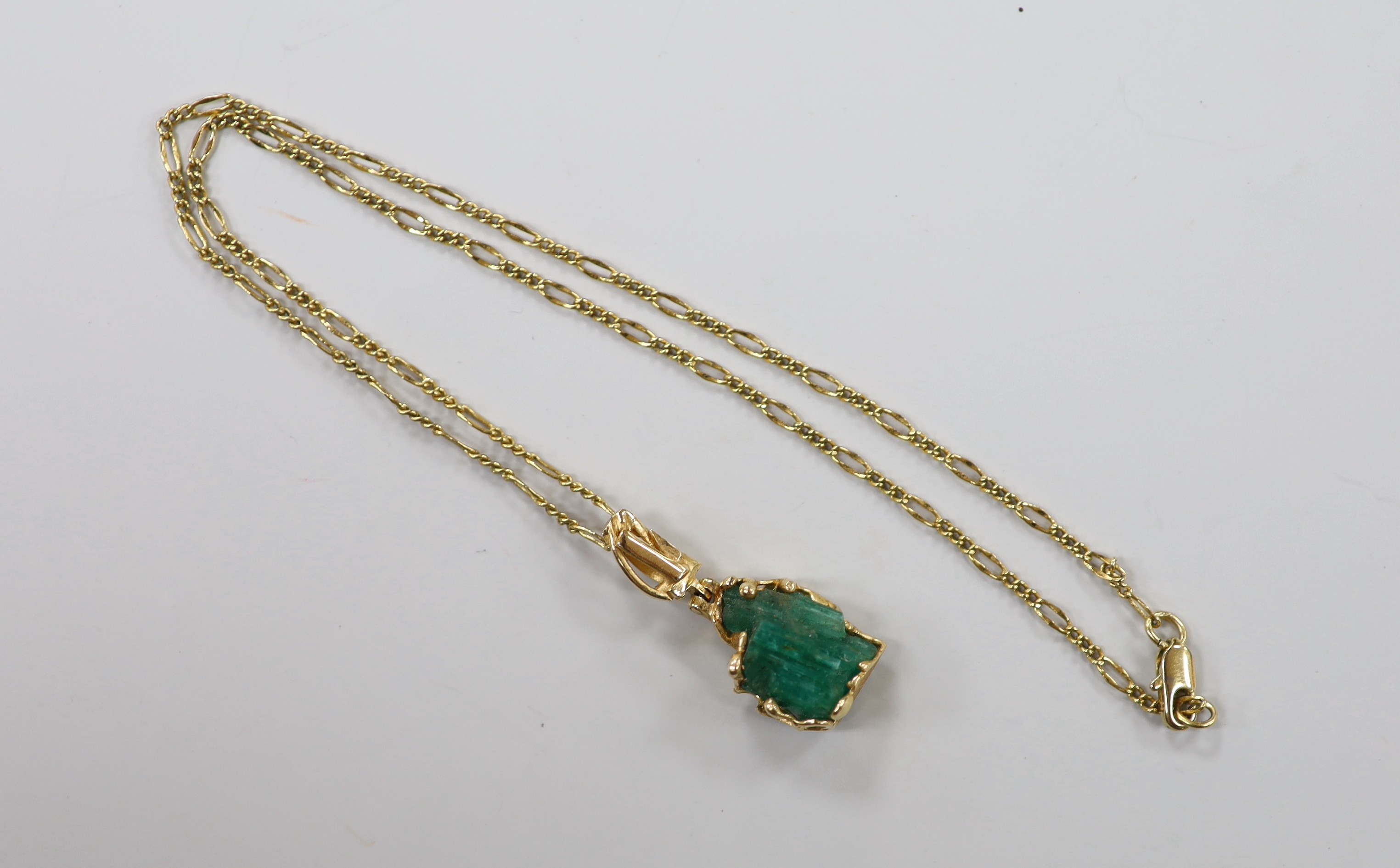 A yellow metal mounted carved emerald boulder set pendant, overall 34mm, gross weight 6 grams, on a gilt metal chain.